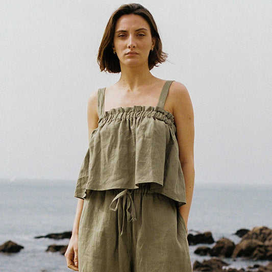 Frau in olivgrünem Leinen-Top und Hose am Strand, Sommermode, lässiger Stil.