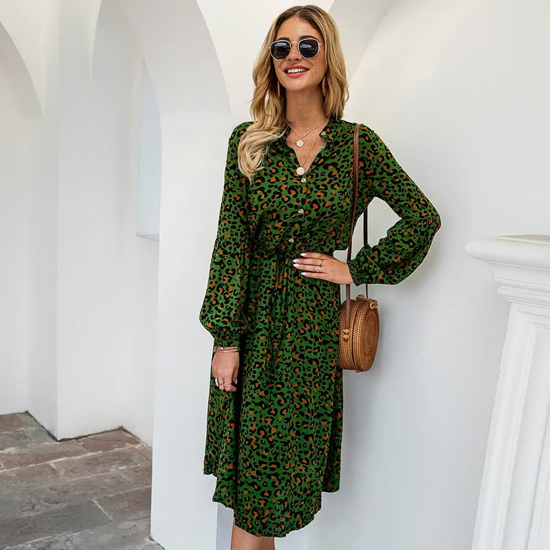 Frau in grünem Leopardenkleid mit Sonnenbrille und brauner Umhängetasche vor weißem Hintergrund.