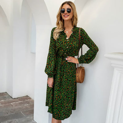 Frau in grünem Leopardenkleid mit Sonnenbrille und brauner Umhängetasche vor weißem Hintergrund.