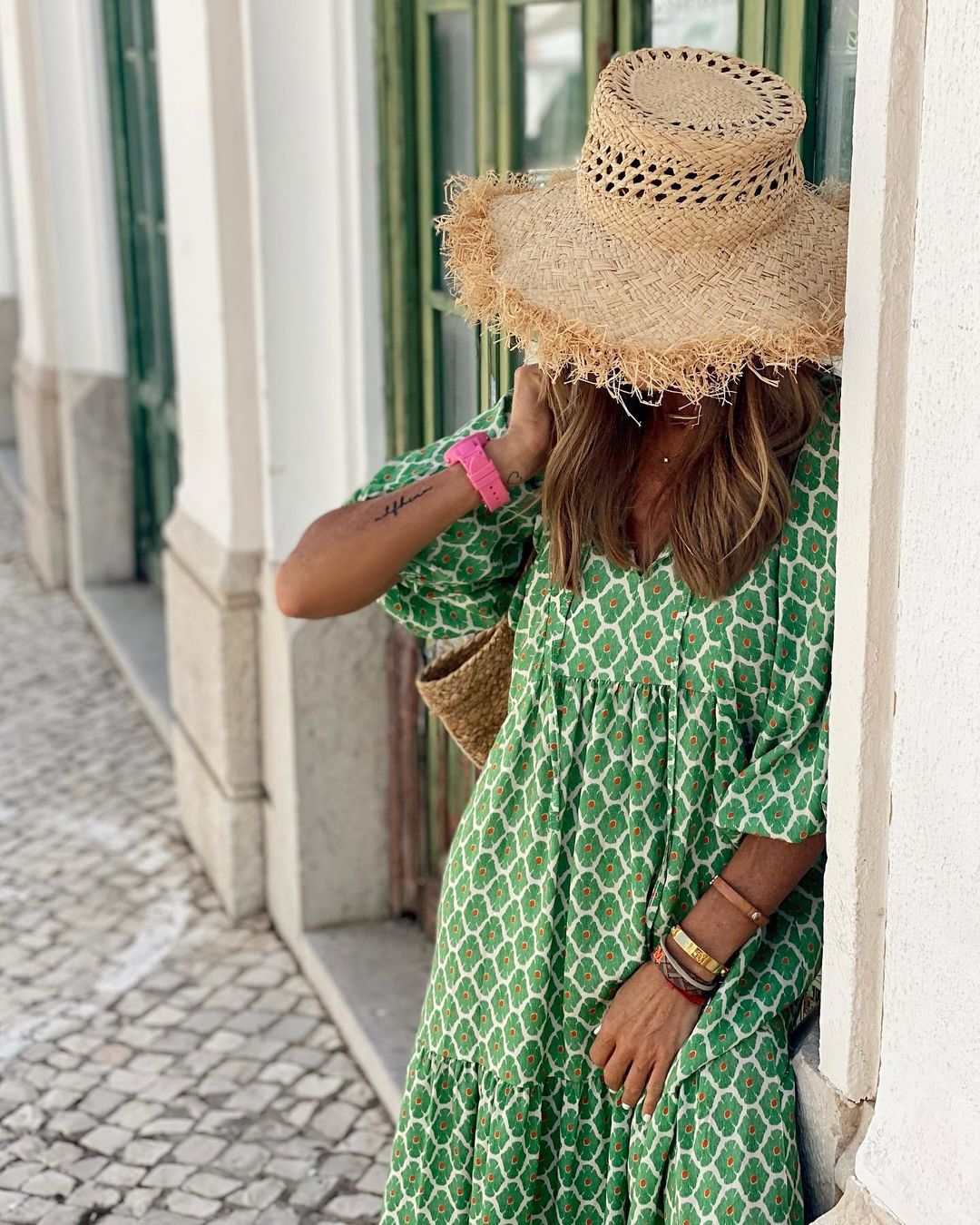 Frau in grünem Kleid und Strohhut lehnt an Wand, Sommermode, lässiger Stil, Outdoor.