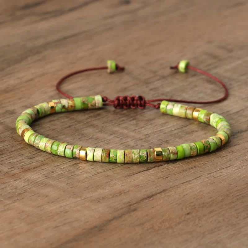 Grünes Perlenarmband aus Naturstein mit verstellbarem braunem Band auf Holzoberfläche.
