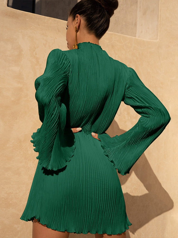 Frau in grünem, plissiertem Minikleid mit langen Ärmeln, elegantes Design, Rückansicht.