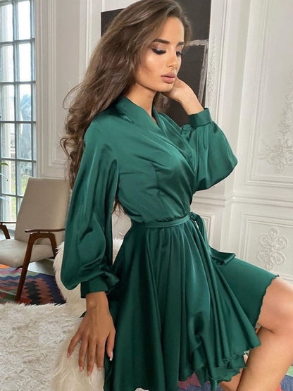 Frau in elegantem, grünem Satin-Kleid mit langen Ärmeln, sitzt stilvoll im Wohnzimmer.