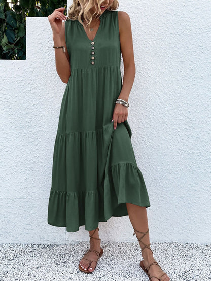 Frau in grünem Sommerkleid mit Knopfleiste, Sandalen, vor weißer Wand.