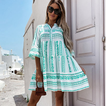 Frau in weißem und grünem Sommerkleid mit geometrischem Muster, steht vor mediterraner Kulisse.