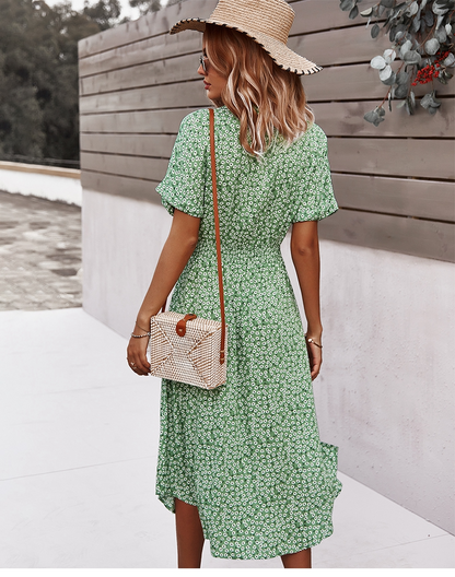 Frau im grünen Sommerkleid mit Strohhut und Korbtasche vor Holzwand.