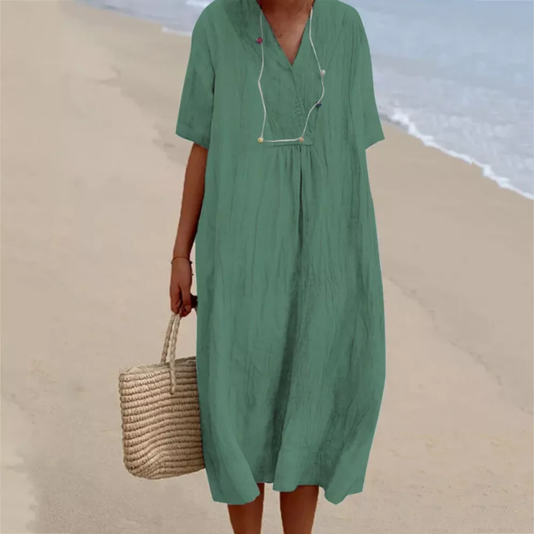 Frau in grünem Leinenkleid am Strand mit Strohtasche, Sommermode, lässiger Stil.