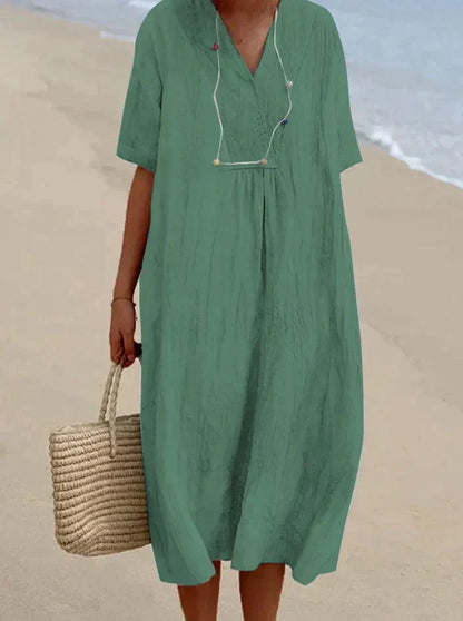 Frau im grünen Leinenkleid am Strand mit Strohtasche, Sommermode, lässiger Stil.