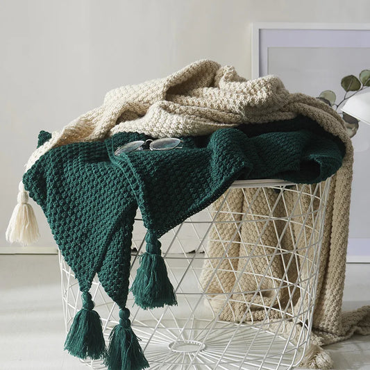 Grüner Strickplaid mit Quasten auf weißem Drahtkorb, dekorative Decke, Wohnzimmer Accessoire.
