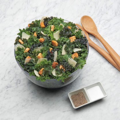 Grüner Salat mit Croutons und Parmesan in Glasschüssel auf Marmortisch, Holzlöffel daneben.