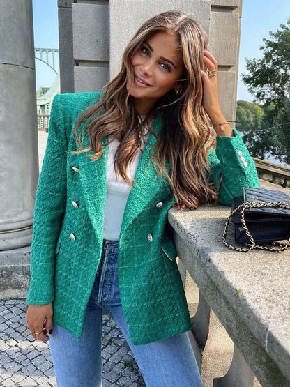 Frau in grünem Blazer, weißem Top, blauen Jeans, posiert draußen, modisch, elegant.
