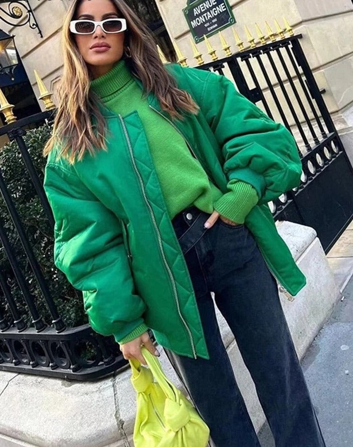 Frau in grüner Bomberjacke, grüner Pullover, schwarze Jeans, gelbe Tasche, Sonnenbrille.