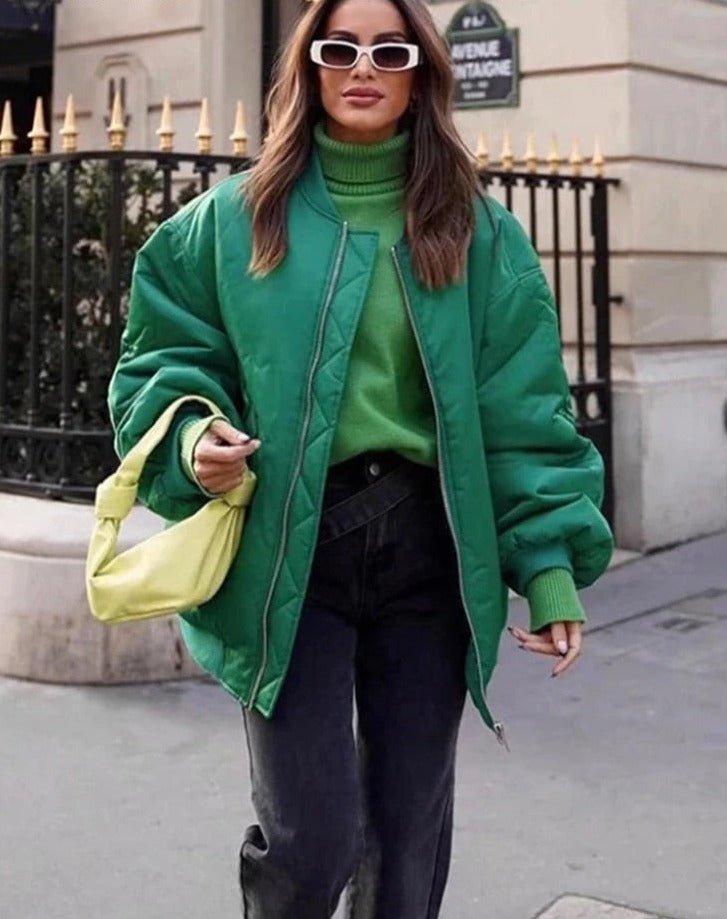 Frau in grüner Bomberjacke, grüner Rollkragenpullover, schwarze Jeans, gelbe Handtasche, Sonnenbrille.