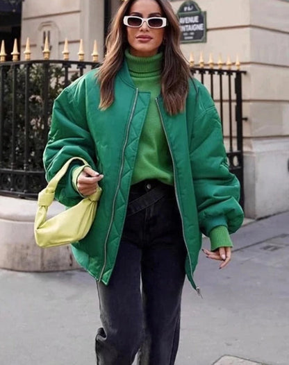 Frau in grüner Bomberjacke, grüner Rollkragenpullover, schwarze Jeans, gelbe Handtasche, Sonnenbrille.