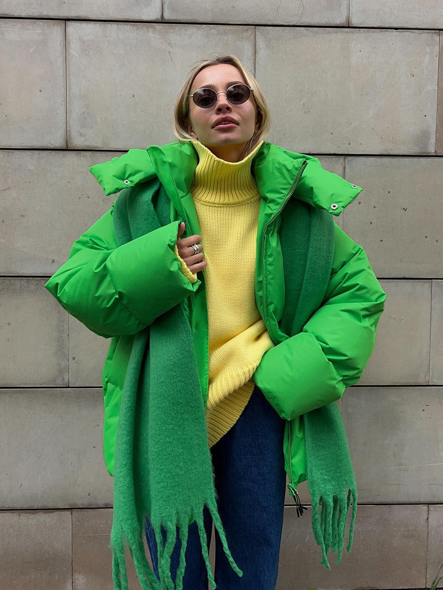Frau in grüner Daunenjacke, gelbem Rollkragenpullover, grüner Schal, Sonnenbrille, Jeans.