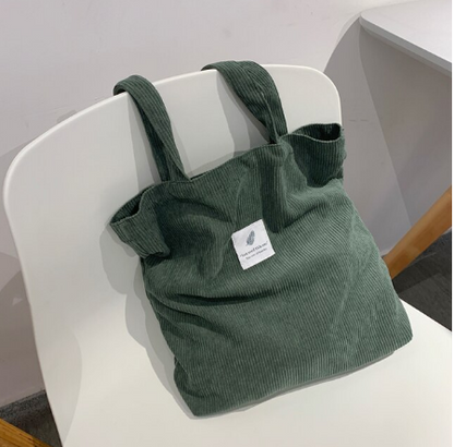 Grüne Cordtasche auf weißem Stuhl, umweltfreundlich, modisch, wiederverwendbar, Einkaufstasche.