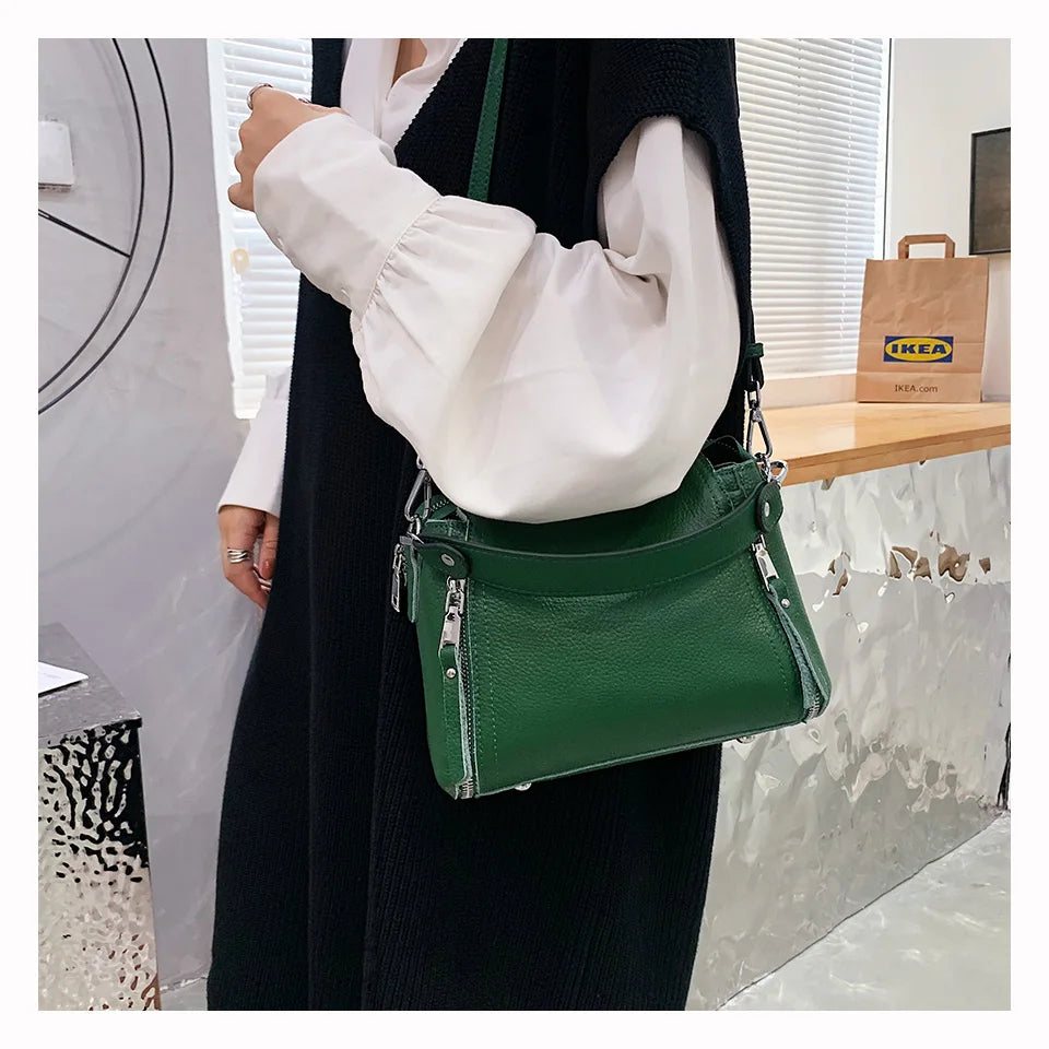 Grüne Ledertasche mit Reißverschlüssen, getragen von Person in schwarzem Outfit, IKEA-Tüte im Hintergrund.