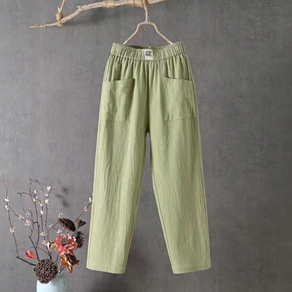 Grüne Leinenhose mit Taschen, Damenmode, lässig, bequem, hängend an Ast, grauer Hintergrund.