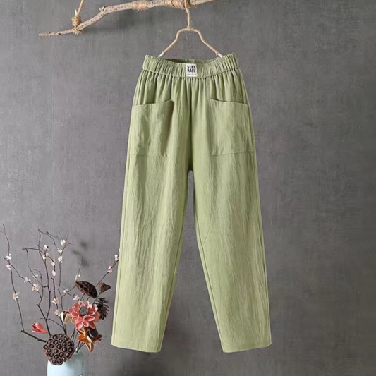 Grüne Leinenhose mit Taschen, Damenmode, lässig, bequem, hängend an Ast, grauer Hintergrund.