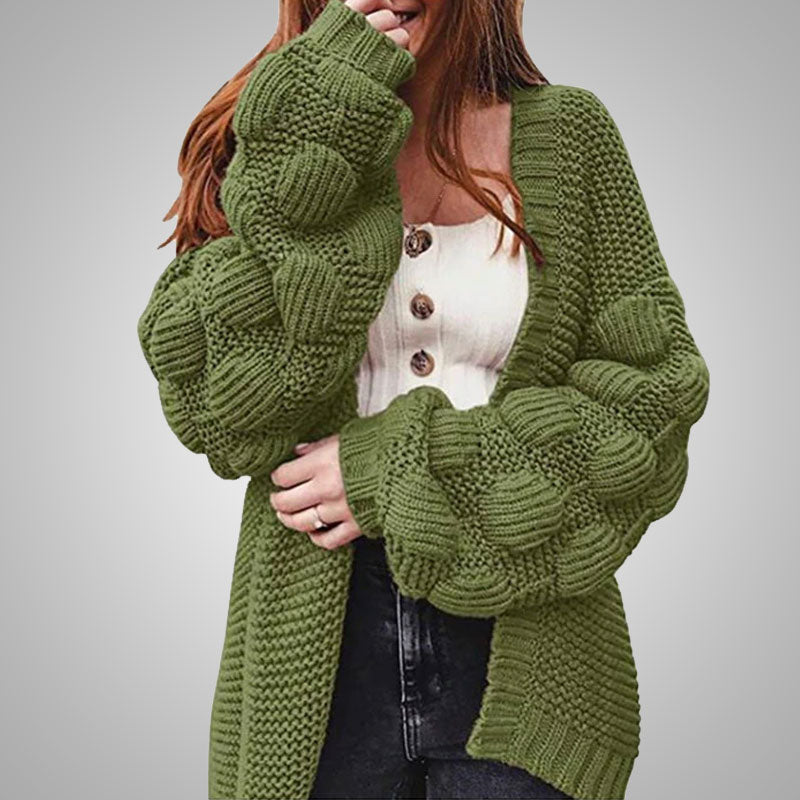 Frau trägt grünen Strickcardigan mit Puffärmeln, weißes Oberteil, schwarze Jeans.