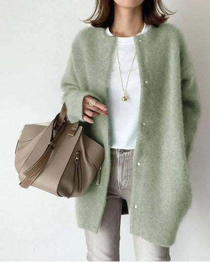 Frau in grüner Strickjacke, weißem T-Shirt, grauer Jeans, beige Handtasche, modisch, elegant.