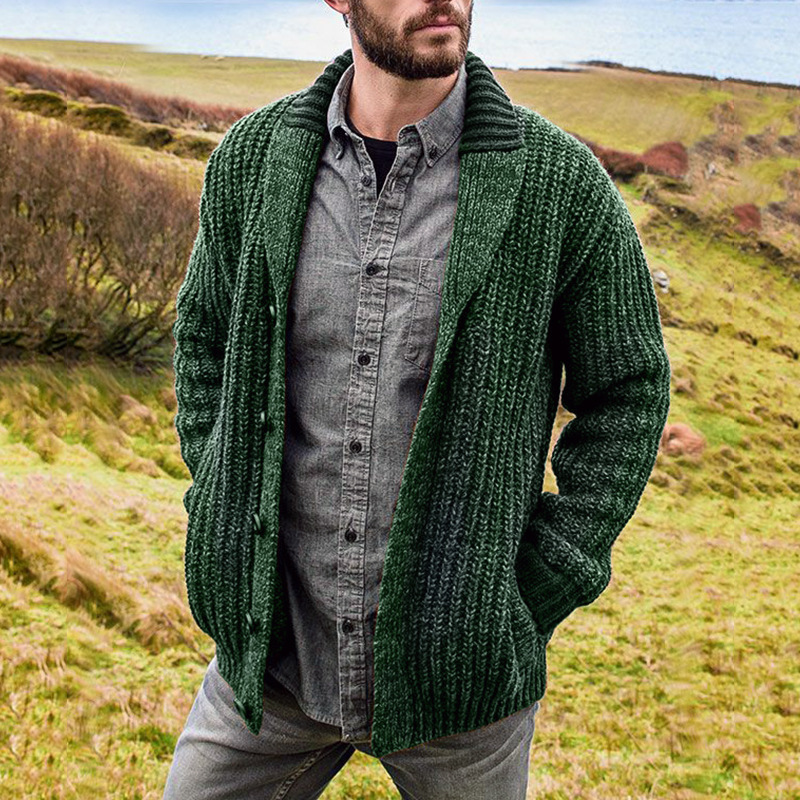 Mann in grüner Strickjacke aus Wolle, lässig über grauem Hemd, Landschaft im Hintergrund.