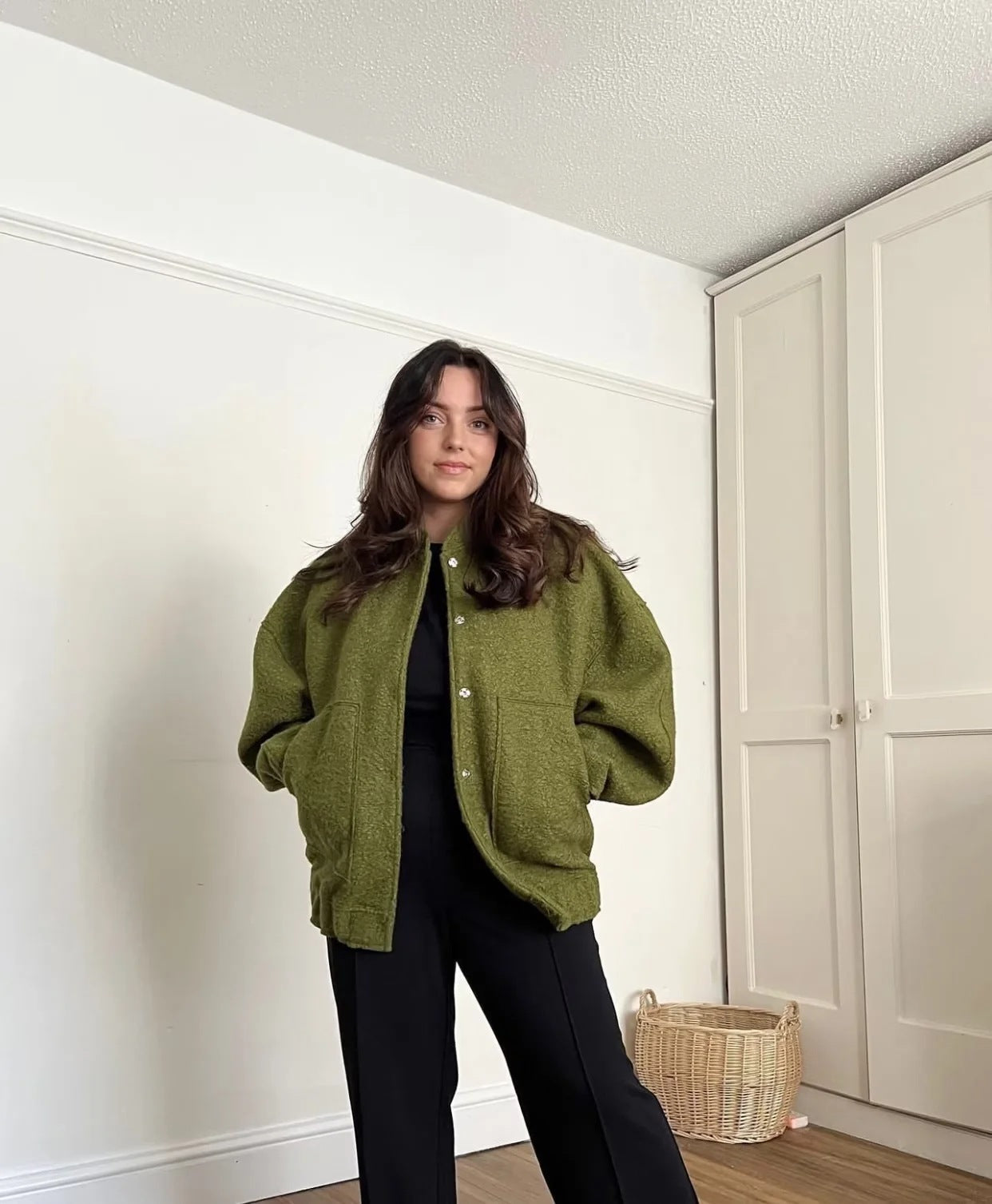 Frau in olivgrüner Wolljacke, schwarze Hose, moderne Mode, Innenraum, Herbstoutfit.