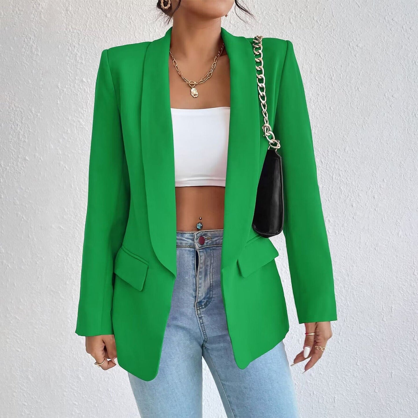 Frau in grünem Blazer, weißem Top, blauer Jeans, goldene Kette, schwarze Tasche.