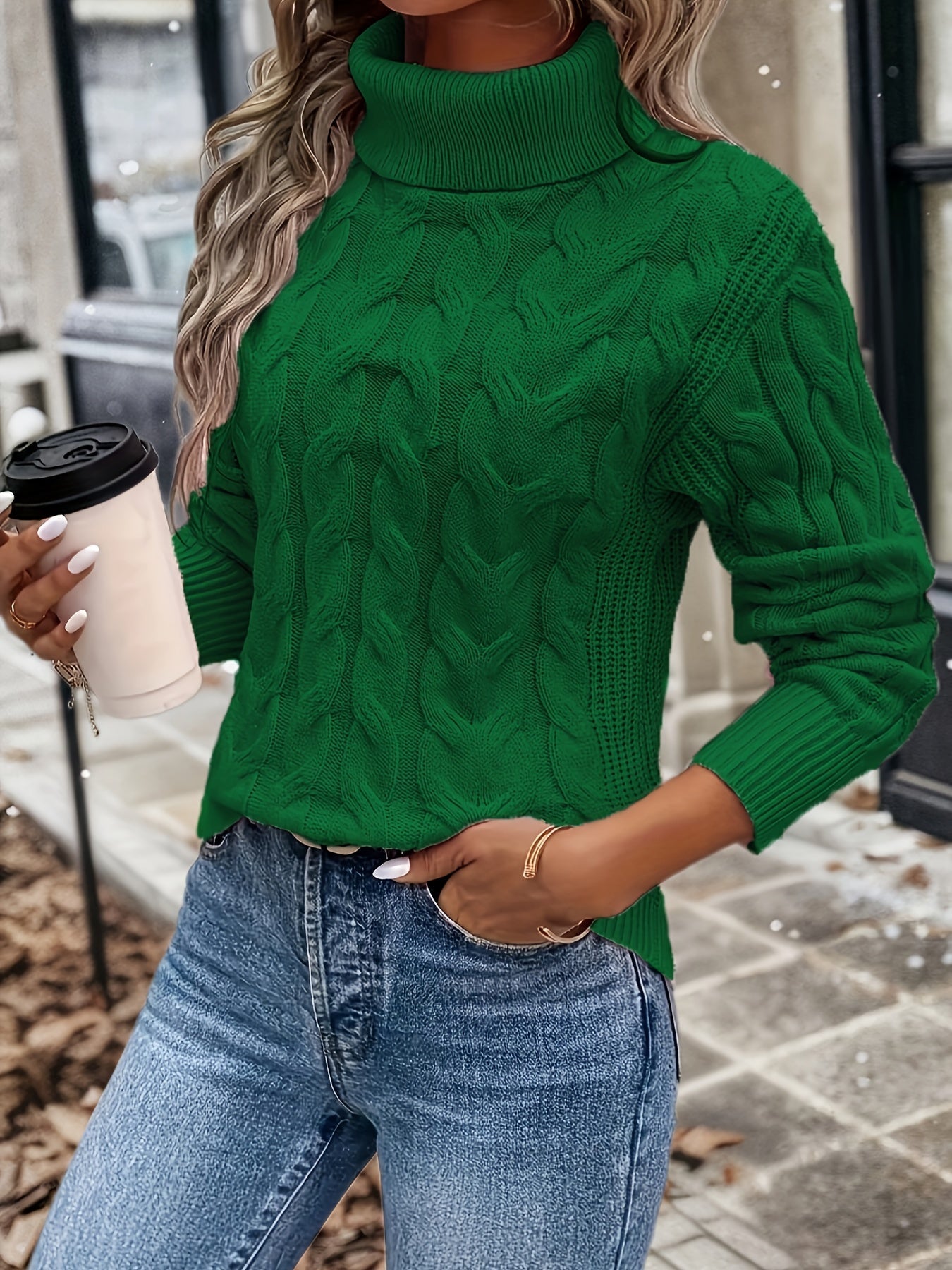 Frau in grünem Rollkragenpullover, hält Kaffeebecher, trägt blaue Jeans, Herbstmode.
