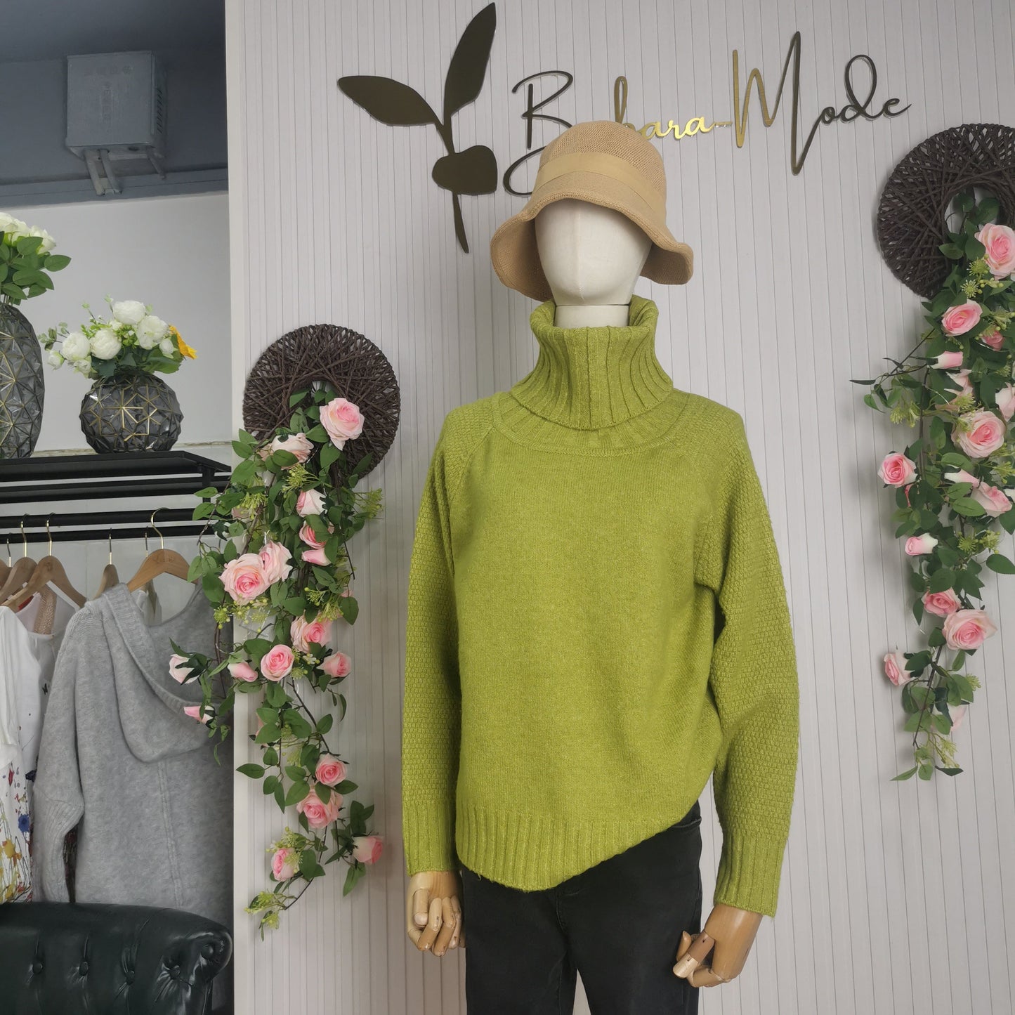 Grüne Strickpullover auf Schaufensterpuppe mit Rollkragen, beige Hut, Modegeschäft-Dekoration.