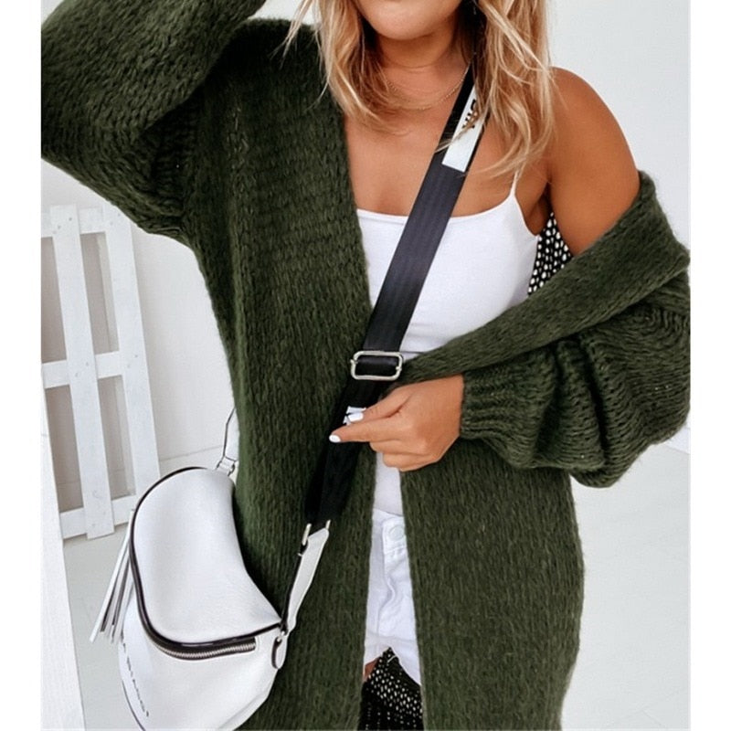 Frau in grünem Strickcardigan mit weißer Umhängetasche und schwarzem Riemen.