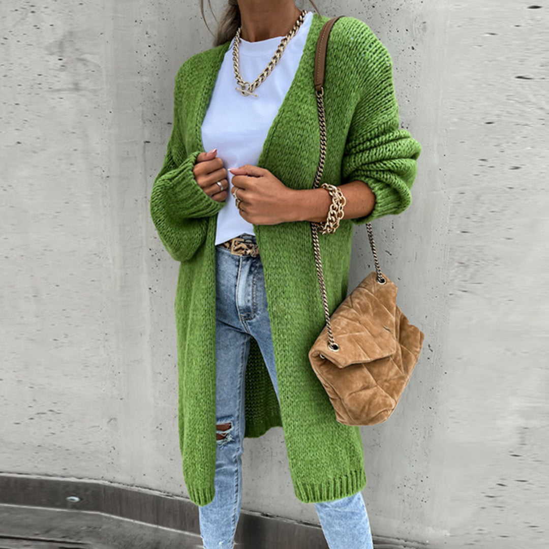 Frau in grünem Strickcardigan, weißem T-Shirt, Jeans, mit brauner Tasche und Goldkette.