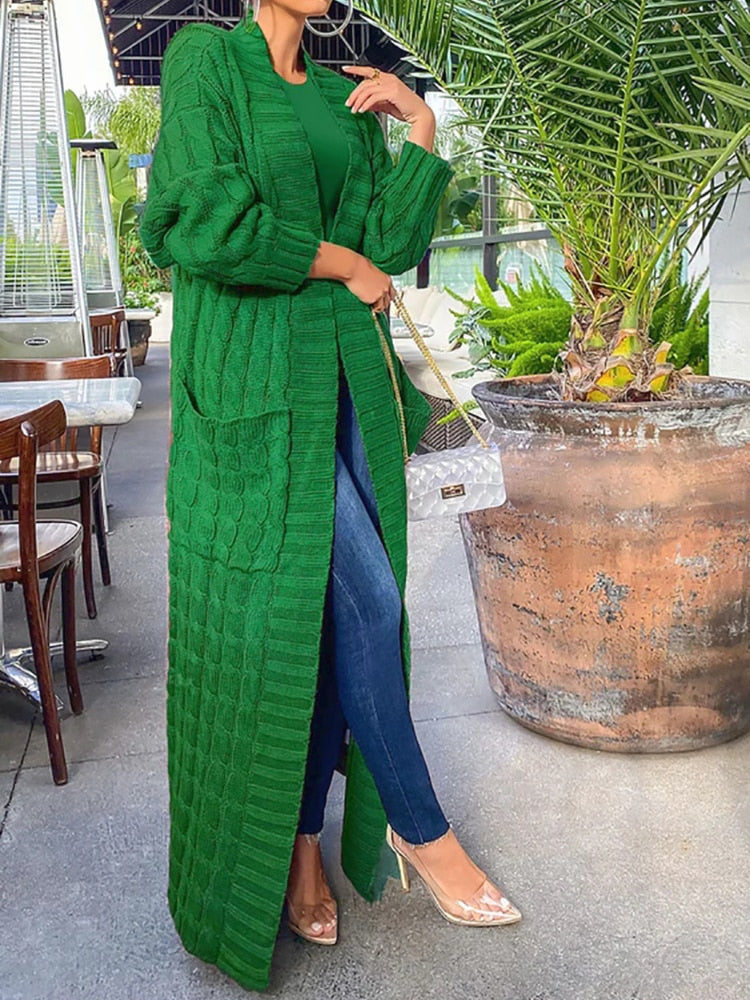Frau in langem, grünem Strickmantel, Jeans und transparenten High Heels in einem Café.
