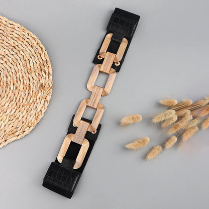 Schwarzer Gürtel mit Holzketten-Elementen, modisches Accessoire, Damenmode, auf grauem Hintergrund.