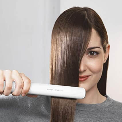 Frau glättet Haare mit weißem Haarglätter, Haarstyling, Glätteisen, Haarpflege, Friseurwerkzeug.
