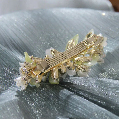Goldene Haarspange mit Blumenmuster, Perlen und Strasssteinen auf grünem Stoff.