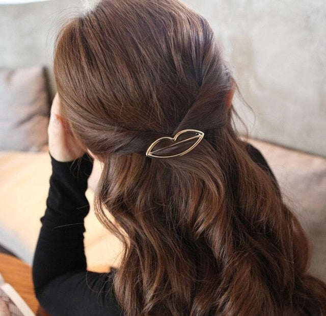 Frau mit braunem Haar, goldene Haarspange in Lippenform, elegantes Accessoire, Rückansicht.