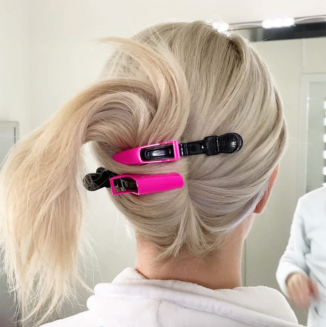 Frau mit blonden Haaren, befestigt mit pinken Haarklammern, im Badezimmer.