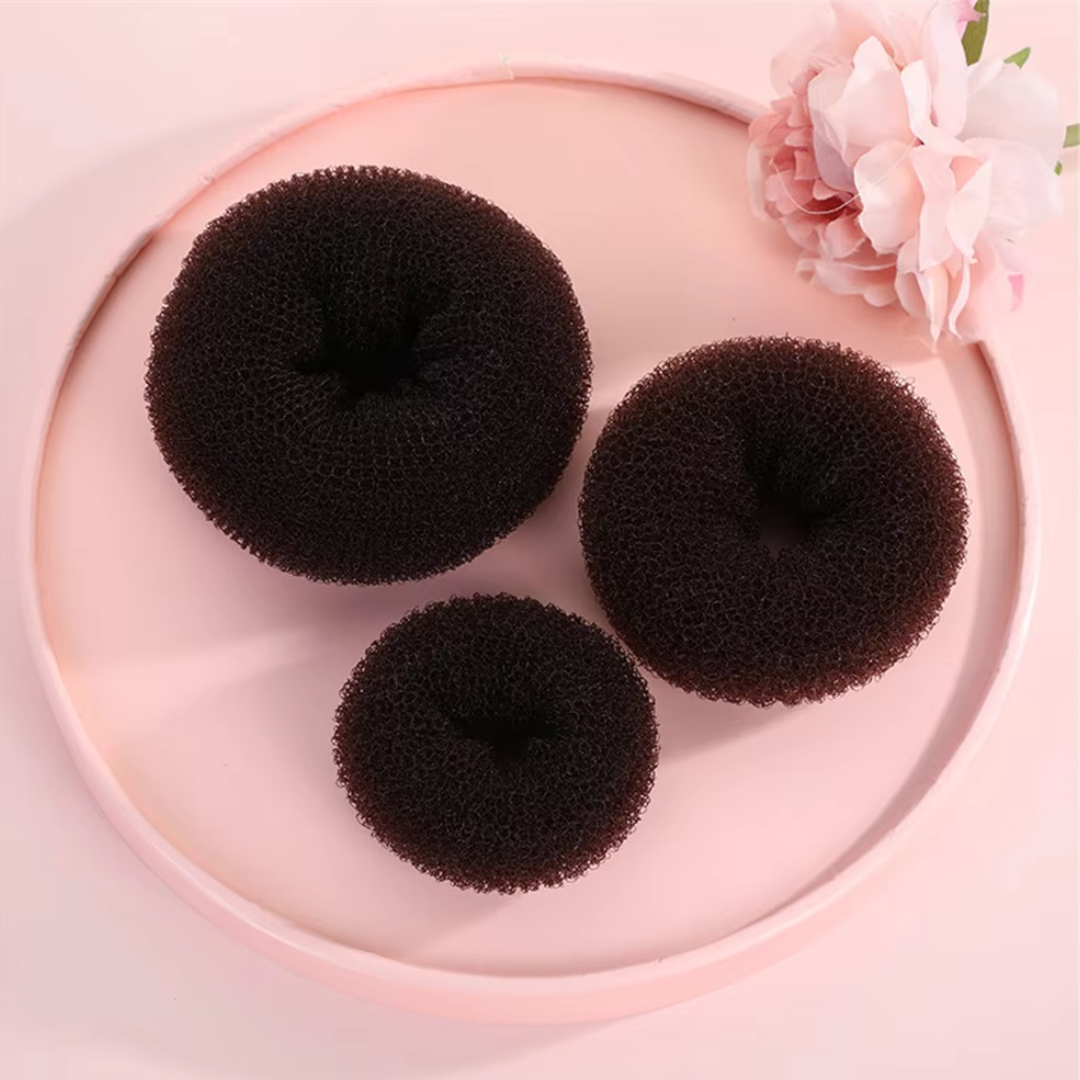 Drei schwarze Haardutts auf rosa Tablett mit Blume, Haarstyling-Accessoires, verschiedene Größen.