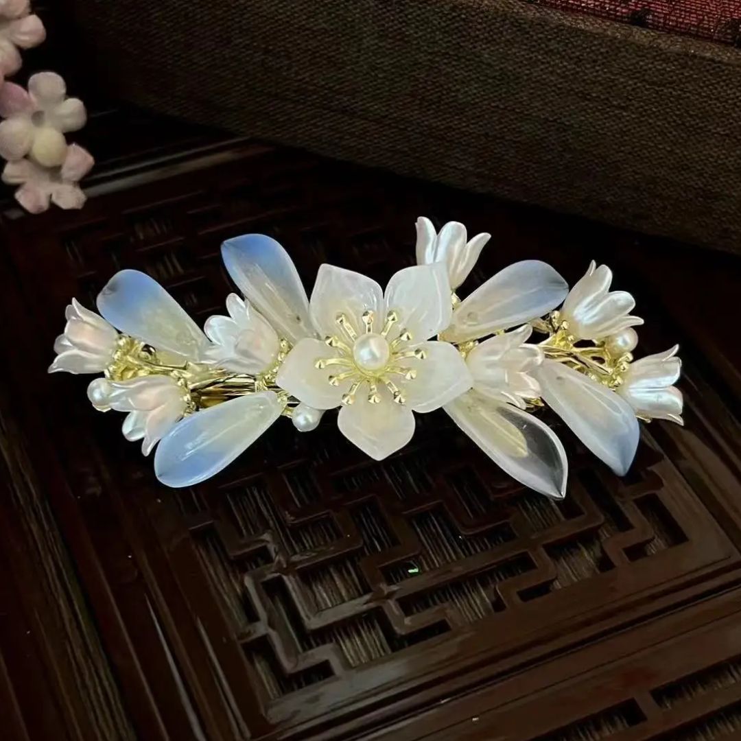 Haarspange mit weißen Blumen, Perlen und goldenen Details auf Holzoberfläche.