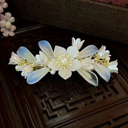 Haarspange mit weißen Blumen, Perlen und goldenen Details auf Holzoberfläche.