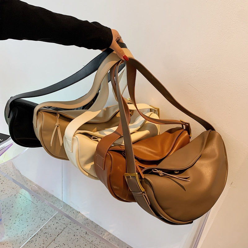 Vier Leder-Umhängetaschen in Schwarz, Weiß, Braun und Beige an einem Arm gehalten.