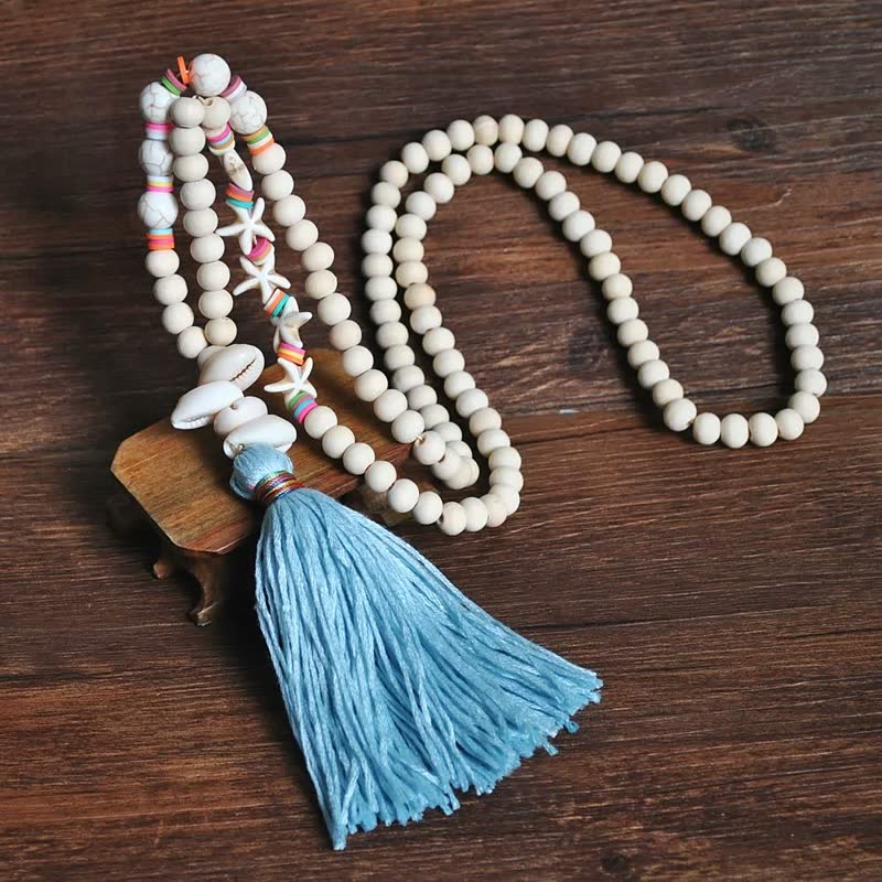 Holzperlenkette mit blauer Quaste und Muscheln auf Holztisch, handgefertigter Schmuck.