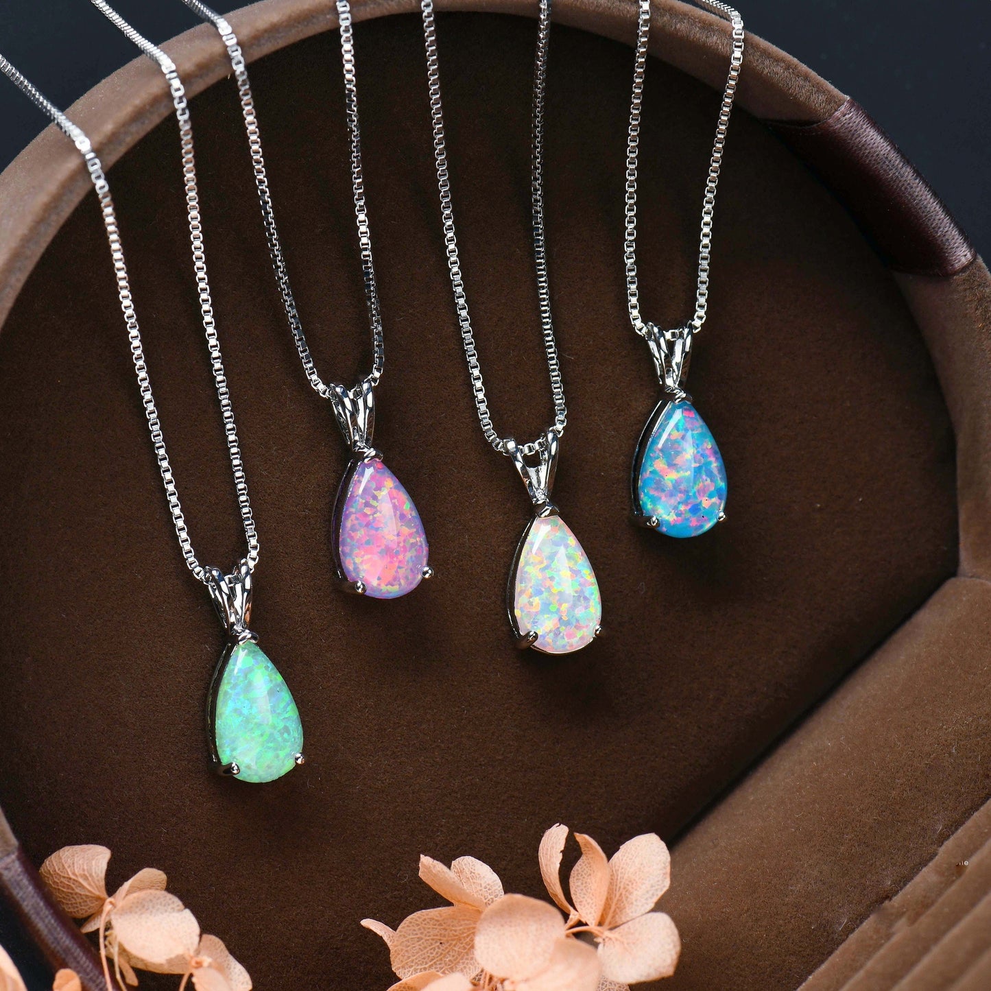 Vier Opal-Anhänger an Silberketten in Schmuckschatulle, bunte Edelsteine, elegantes Design.