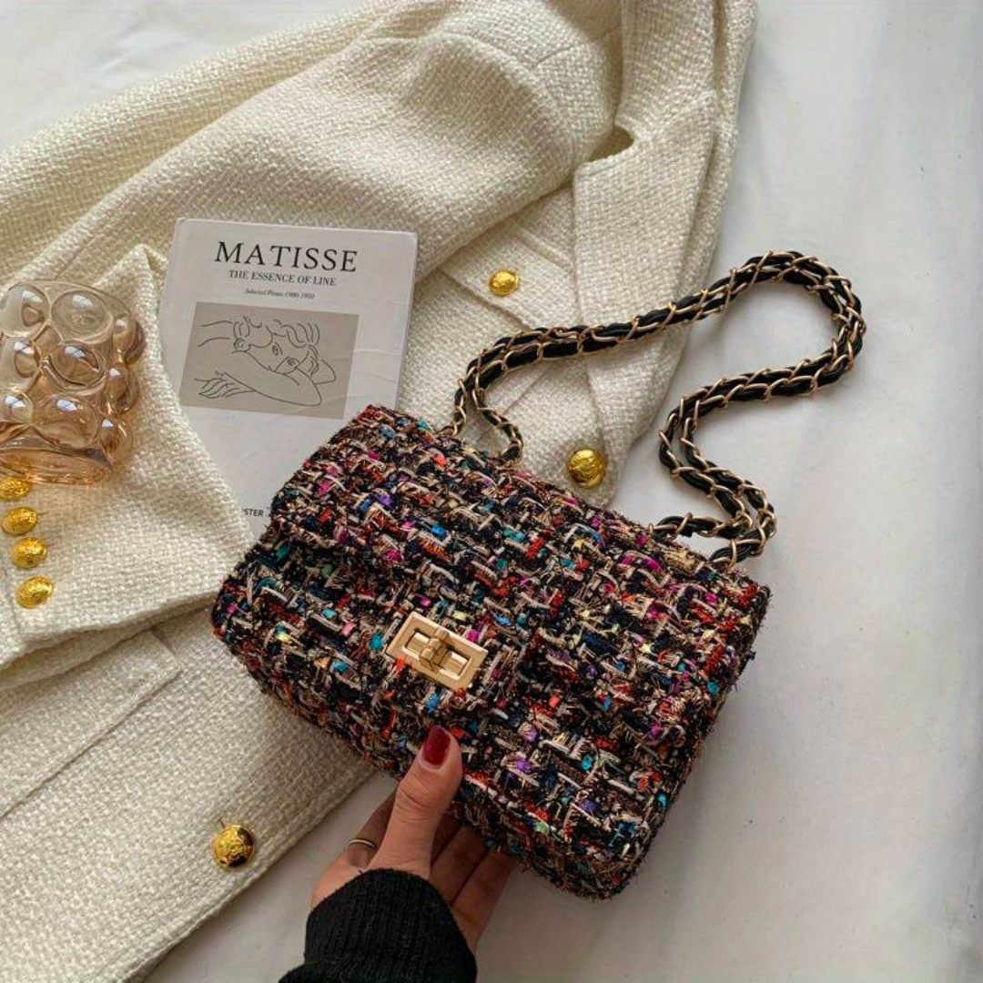 Bunte Tweed-Handtasche mit Kettenriemen auf weißem Mantel, stilvoll und elegant.