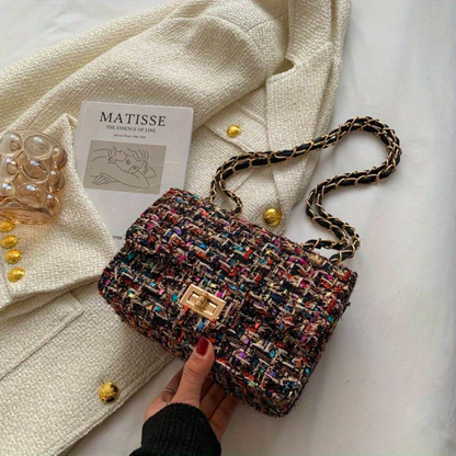 Bunte Tweed-Handtasche mit Kettenriemen auf weißem Mantel, stilvoll und elegant.
