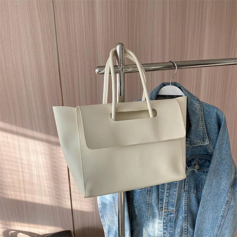 Beige Ledertasche auf Kleiderständer neben blauer Jeansjacke, modisches Accessoire.