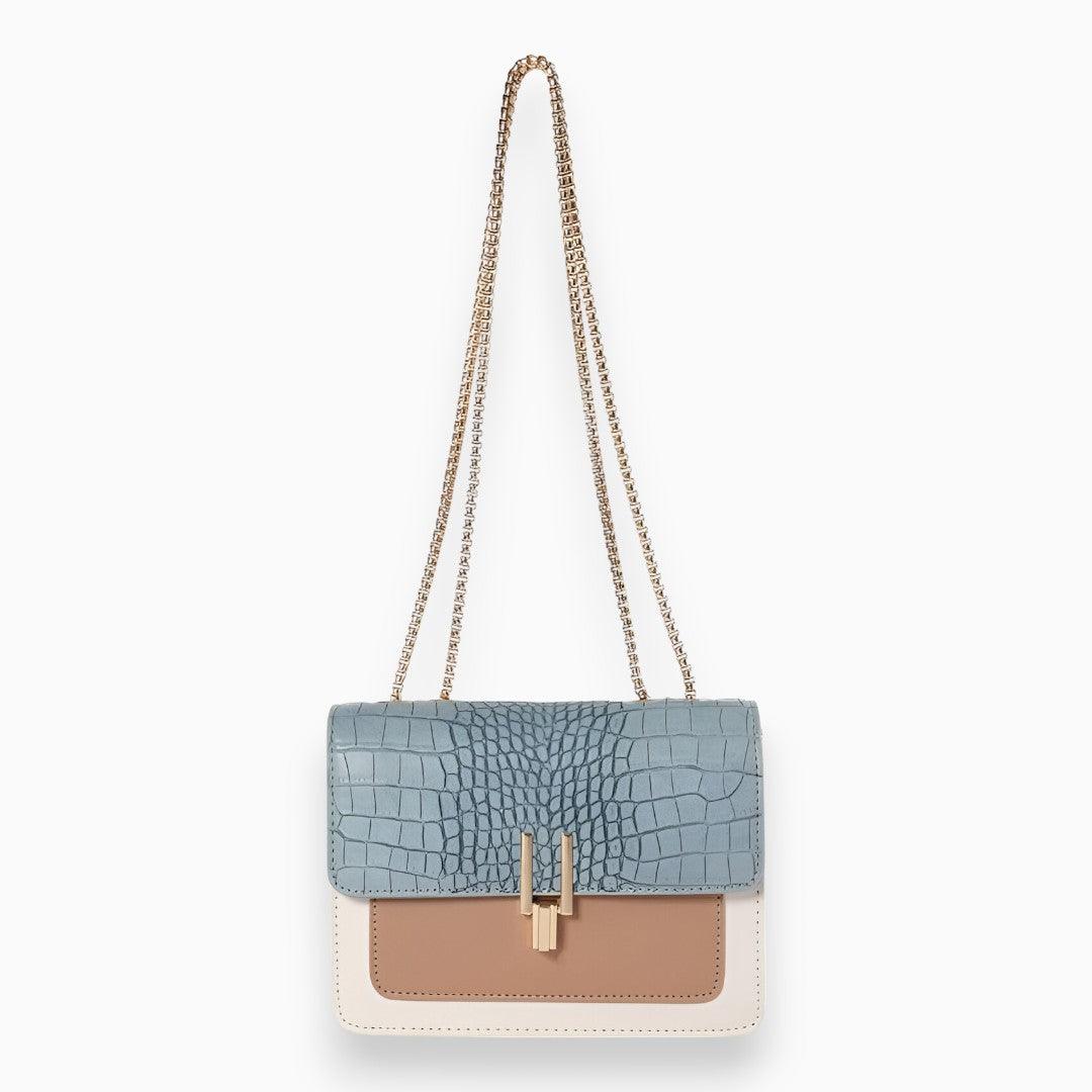Blaue Damenhandtasche mit Krokodilleder-Optik, goldener Kette, beige und weißem Design.