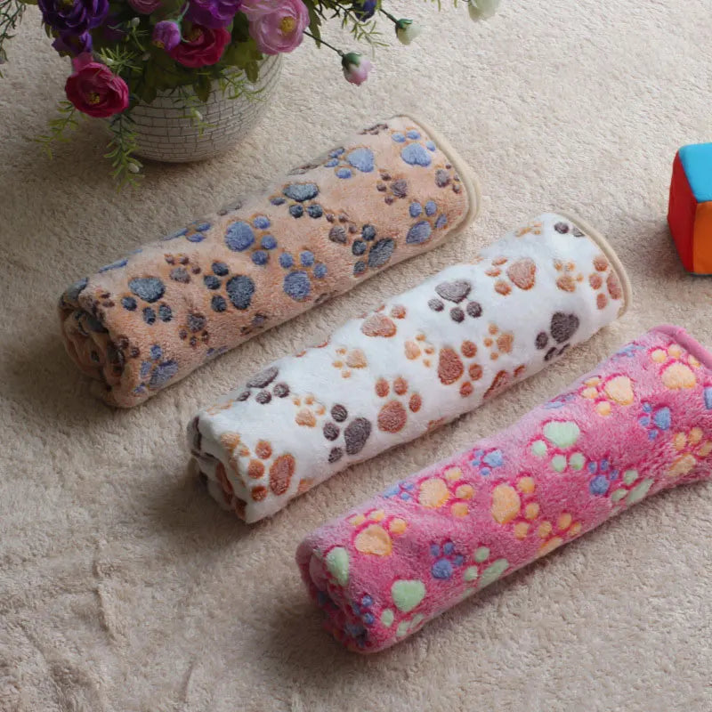 Drei bunte Fleece-Haustierdecken mit Pfotenmuster auf Teppich, ideal für Katzen und Hunde.