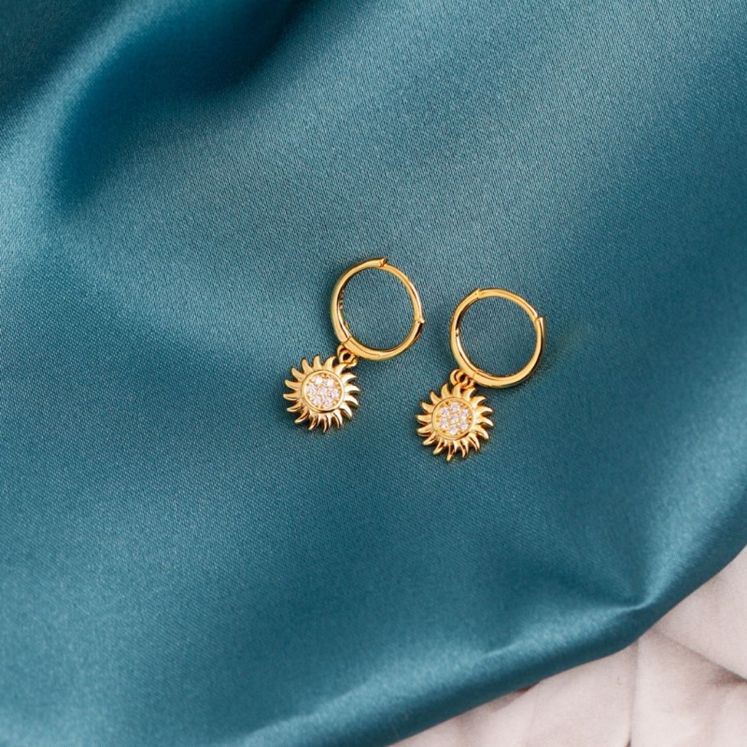 Goldene Sonnen-Creolen-Ohrringe auf blauem Stoff, Schmuck, modisch, elegant.